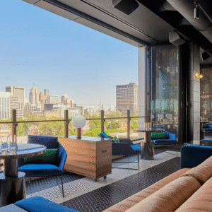 Couple enjoying cocktails on a modern rooftop lounge with city skyline views and ambient lighting, overlooking downtown Detroit at golden hour.