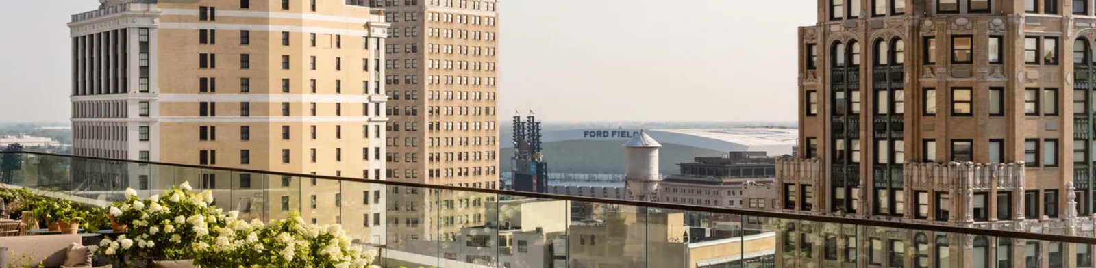 Rooftop terrace at Kamper’s in Detroit featuring elegant lounge seating, lush greenery, and sweeping skyline views including Ford Field and historic downtown buildings.
