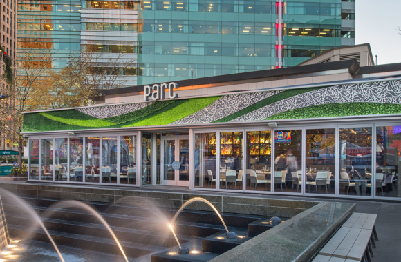 Exterior of Parc restaurant in downtown Detroit featuring a sleek glass façade, vibrant green rooftop design, and views of Campus Martius with a modern fountain in the foreground.