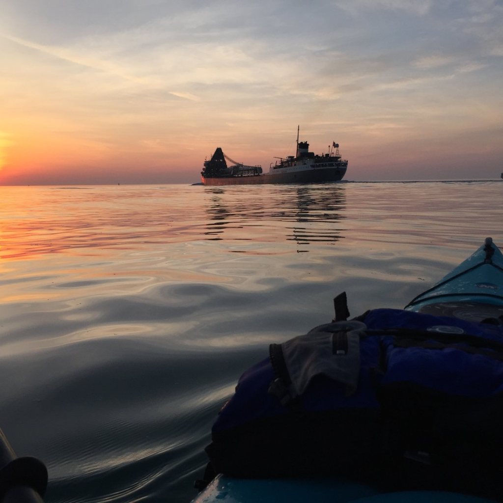 Kayaker on Sunset Canal Tour in Detroit with view of freighter ship and golden hour sky over calm water