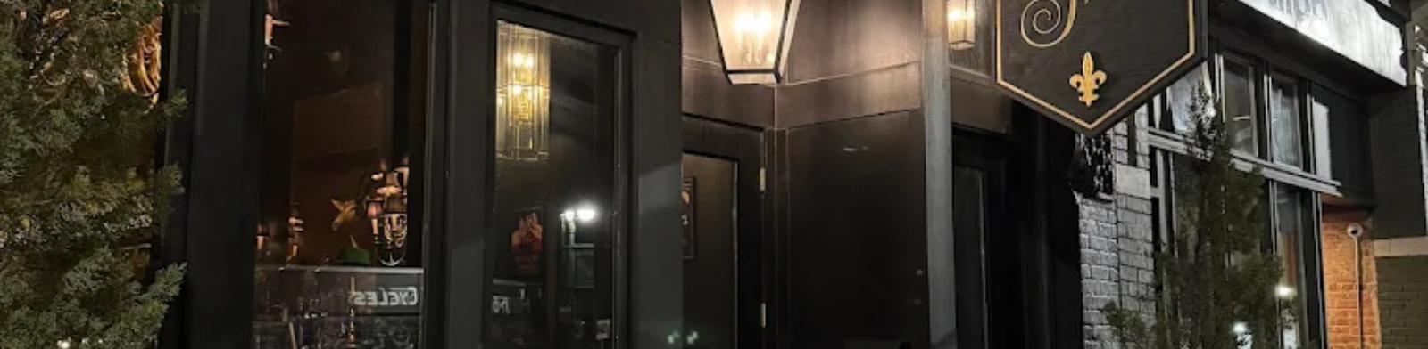 Exterior of The Sugar House in Detroit at night featuring a black façade, warm lantern lighting, and a classic hanging sign, creating an intimate and upscale cocktail bar atmosphere.