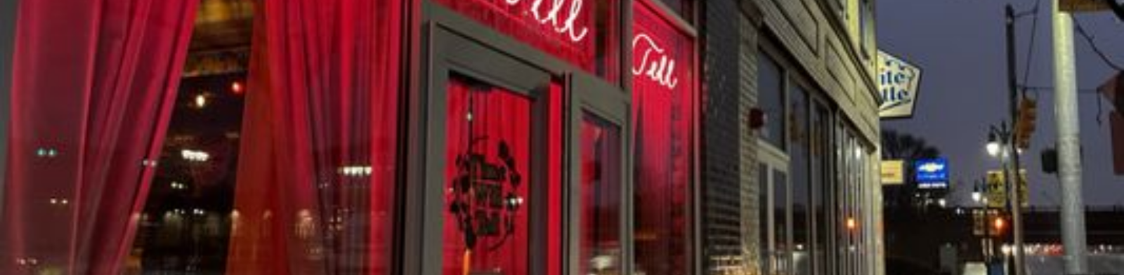 Exterior of Time Will Tell in Detroit at night featuring glowing red neon signage, sheer red curtains, and a moody, intimate cocktail bar entrance along a city street.