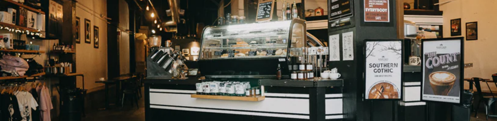 Industrial-style interior of Dessert Oasis Coffee Roasters in Detroit featuring a central coffee bar, pastry display case, exposed ductwork, warm lighting, and a spacious café with modern and vintage elements.