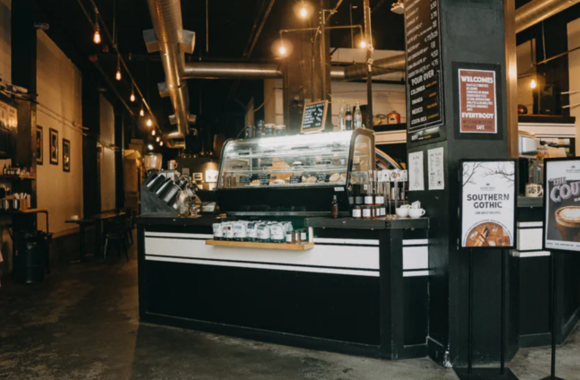 Industrial-style interior of Dessert Oasis Coffee Roasters in Detroit featuring a central coffee bar, pastry display case, exposed ductwork, warm lighting, and a spacious café with modern and vintage elements.