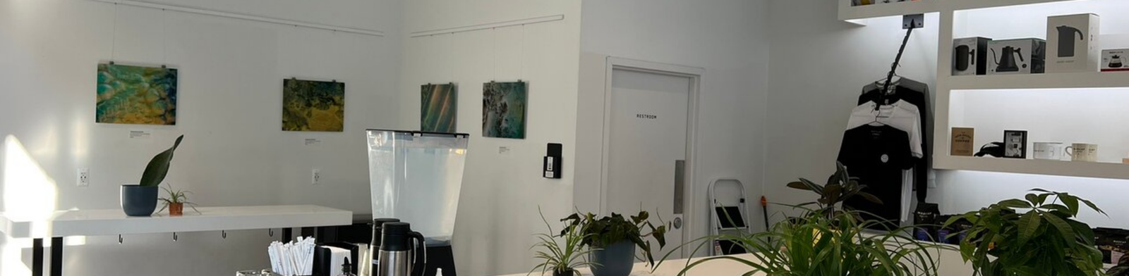 Minimalist interior of Madcap Coffee featuring a clean white coffee bar, modern shelving with coffee products, indoor plants, and a bright, airy café space with contemporary design.