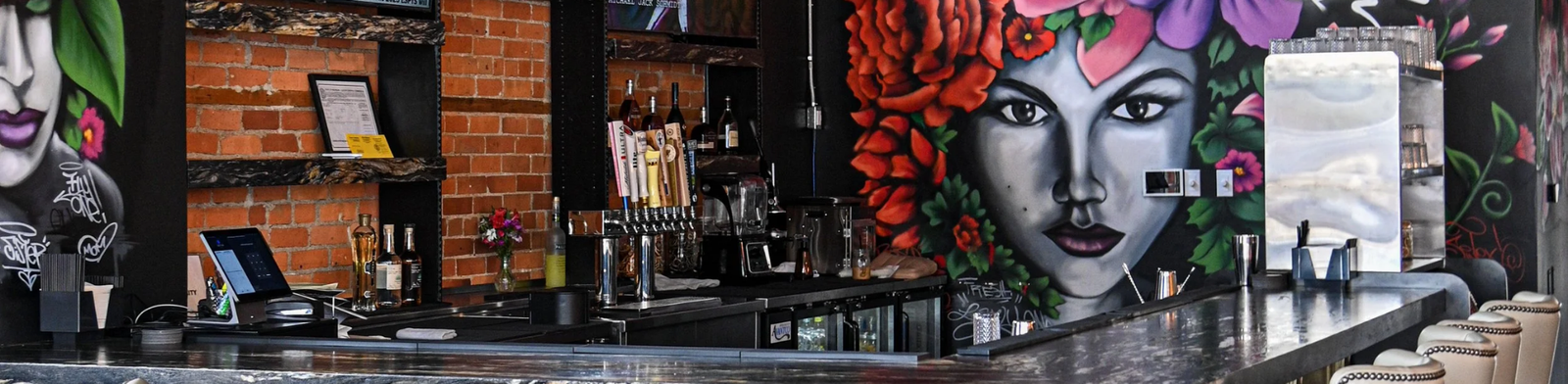 Upscale Detroit bar interior with marble counter seating and a colorful mural of a woman with flowers and “Detroit” graffiti behind the bar.
