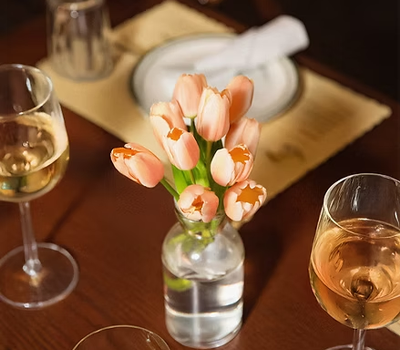 A tulip‑themed wine tasting scene with glasses of wine and vibrant tulips set against a rustic wood backdrop, evoking a springtime, European ambience.