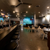 Retro-style interior of UFO Bar in Detroit featuring a long black bar with chrome stools, vintage arcade games, neon signage, and a laid-back neighborhood cocktail atmosphere.
