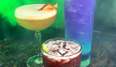 Halloween-themed cocktails at 225 Speakeasy in Atwater Brewery Detroit, featuring red, golden, and purple drinks in a smoky, moody setting.