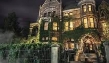 Historic Whitney Mansion in Detroit illuminated at night, covered in ivy with glowing windows and mist rising at the entrance, creating a mysterious haunted ambiance.