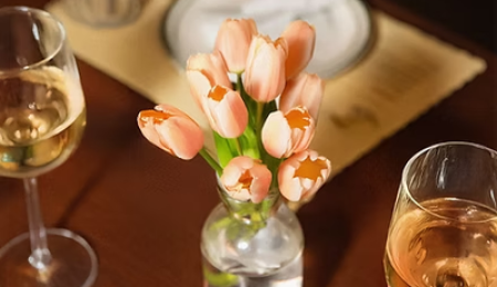 A tulip‑themed wine tasting scene with glasses of wine and vibrant tulips set against a rustic wood backdrop, evoking a springtime, European ambience.